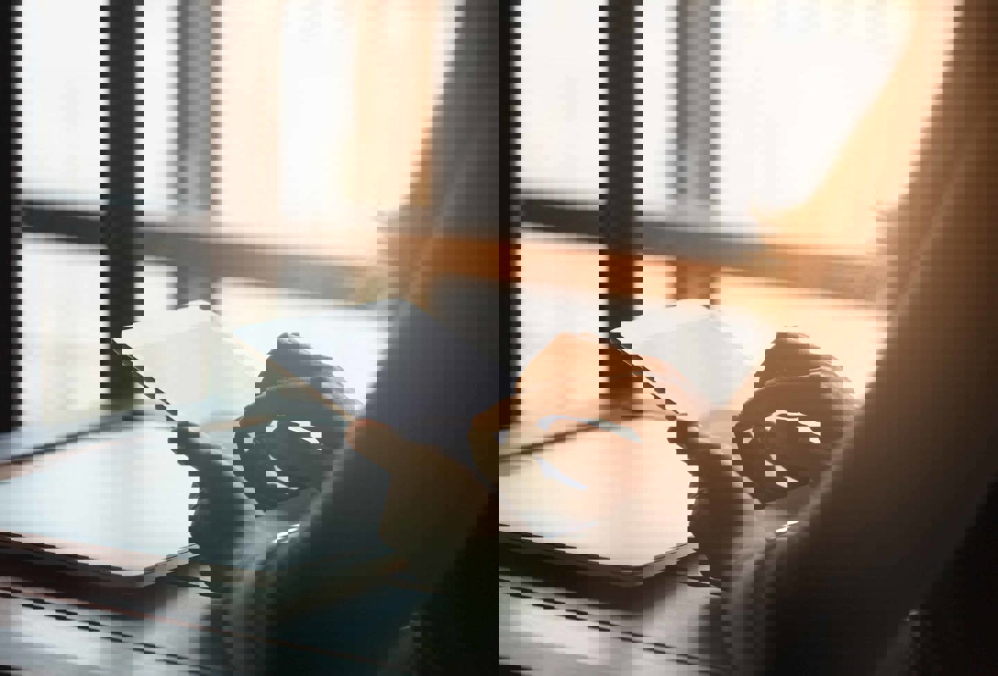 En person læser på sin ipad, indendørs i nærheden af store vinduer, hvor sollyset strømmer ind.