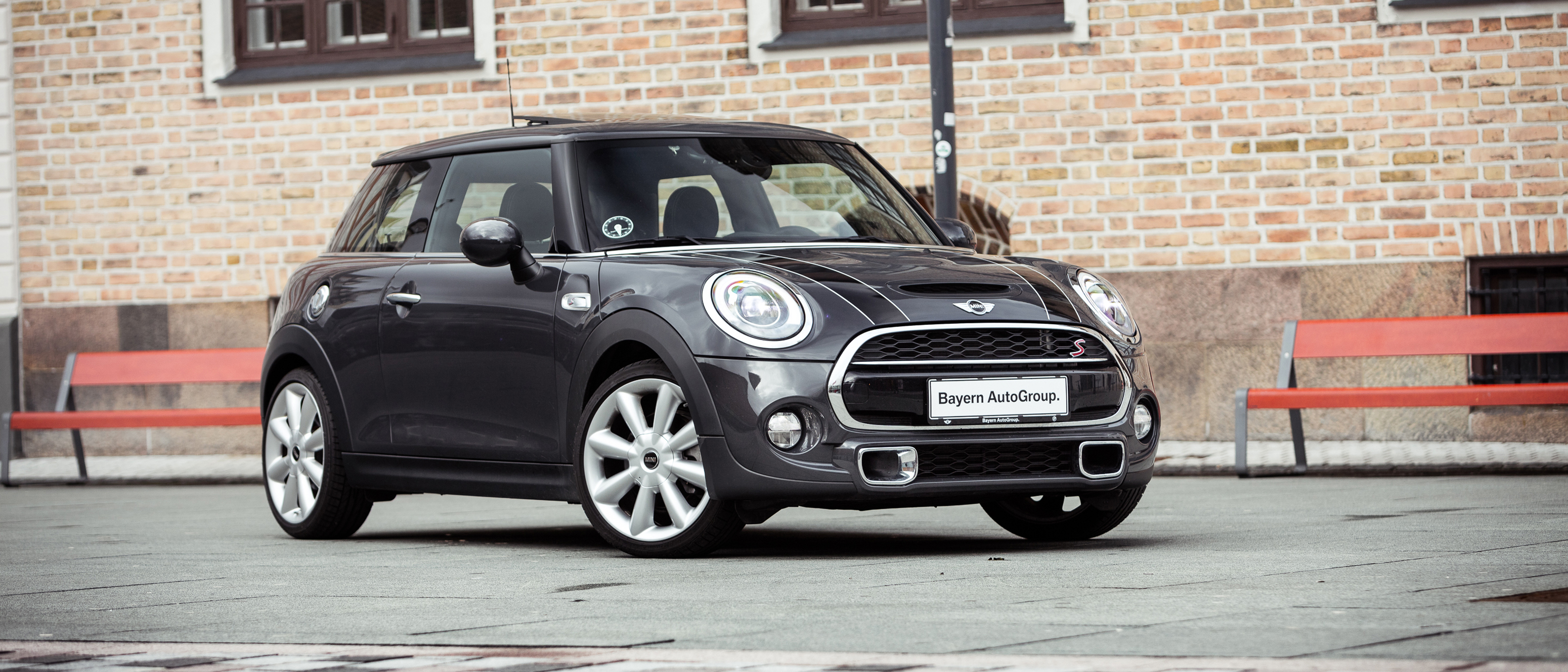 Sort MINI parkeret foran røde bænke 