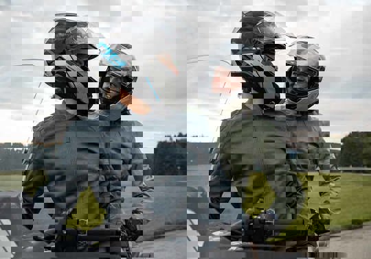 To personer sidder på en parkeret motorcykel med motorcykelhjelm på, mens de kigger på hinanden og smiler.