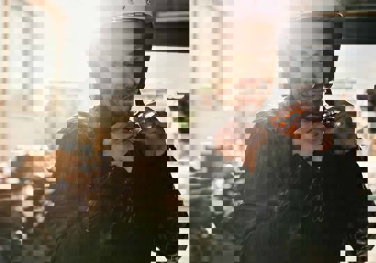 En smilende mand i læderjakke spænder sin motorcykelhjelm, der holder motorcykler parkeret i baggrunden.