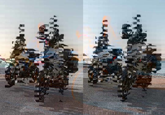 To personer står ved siden af deres BMW Motorcykler, som er parkeret ved en havn.