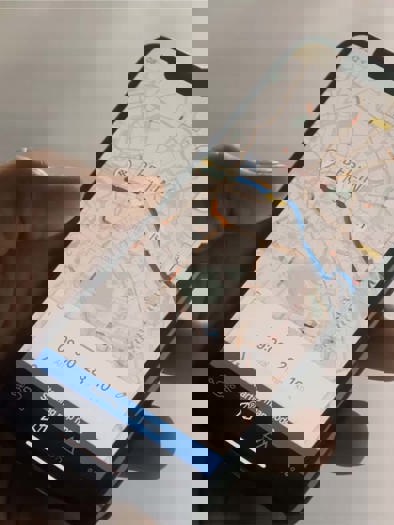 En hånd, der holder en smartphone, viser en kortapplikation med forskellige farverige markører.