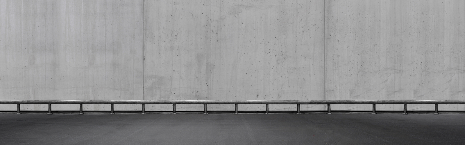 Autoværn i jern foran grå betonmur