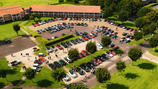 Fyldt parkeringsplads i grønne omgivelser.