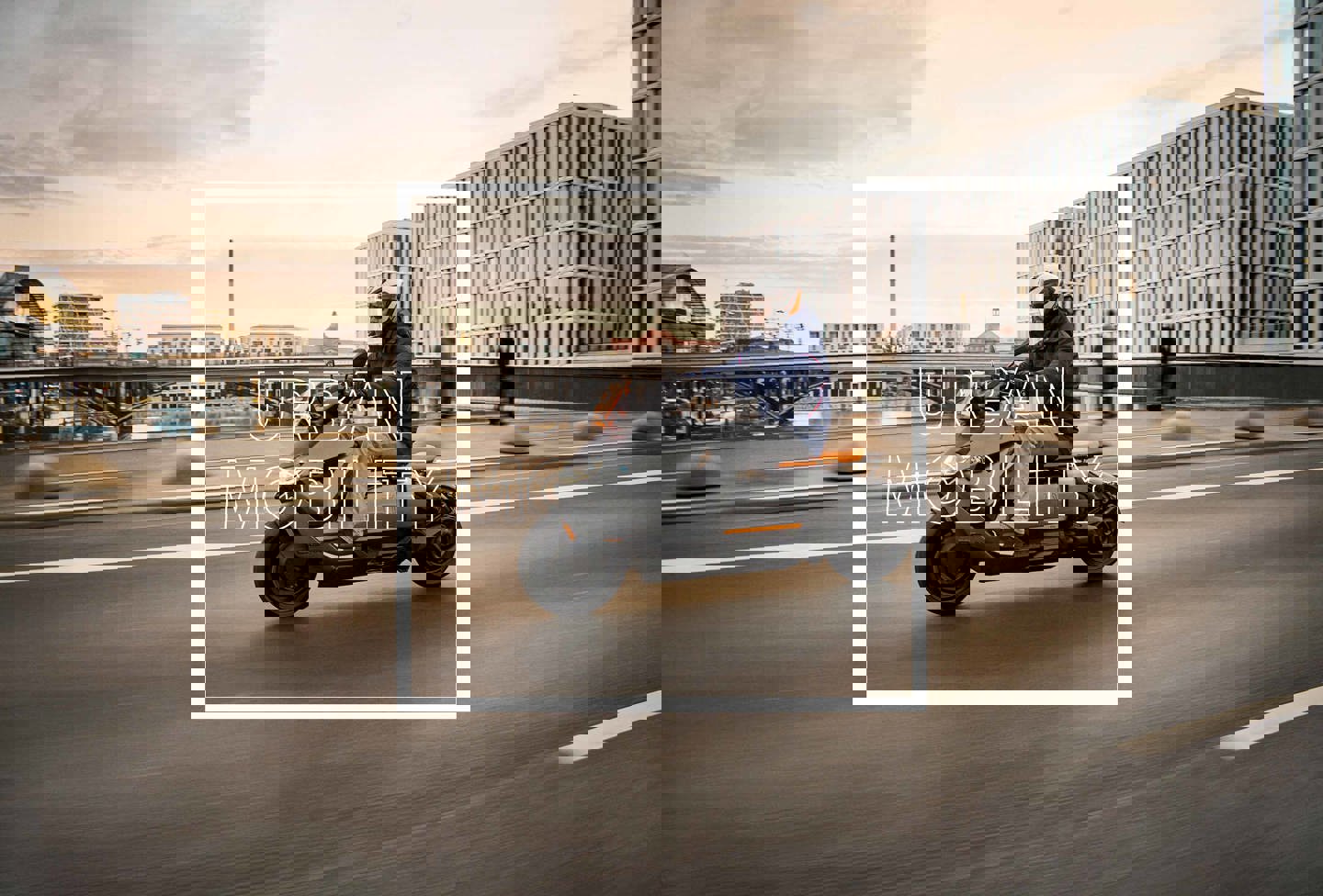 En person kører på en BMW Motorrad Urban motorcykel over en bro i en storby, med bygninger, mennekser og vand i baggrunden. Over billedet står ordene URBAN MOBILITY.
