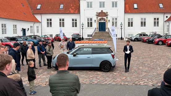 En gruppe mennesker står omkring en lyseblå MINI imens en mand præsenterer den til MINI Spring Drive 2026.