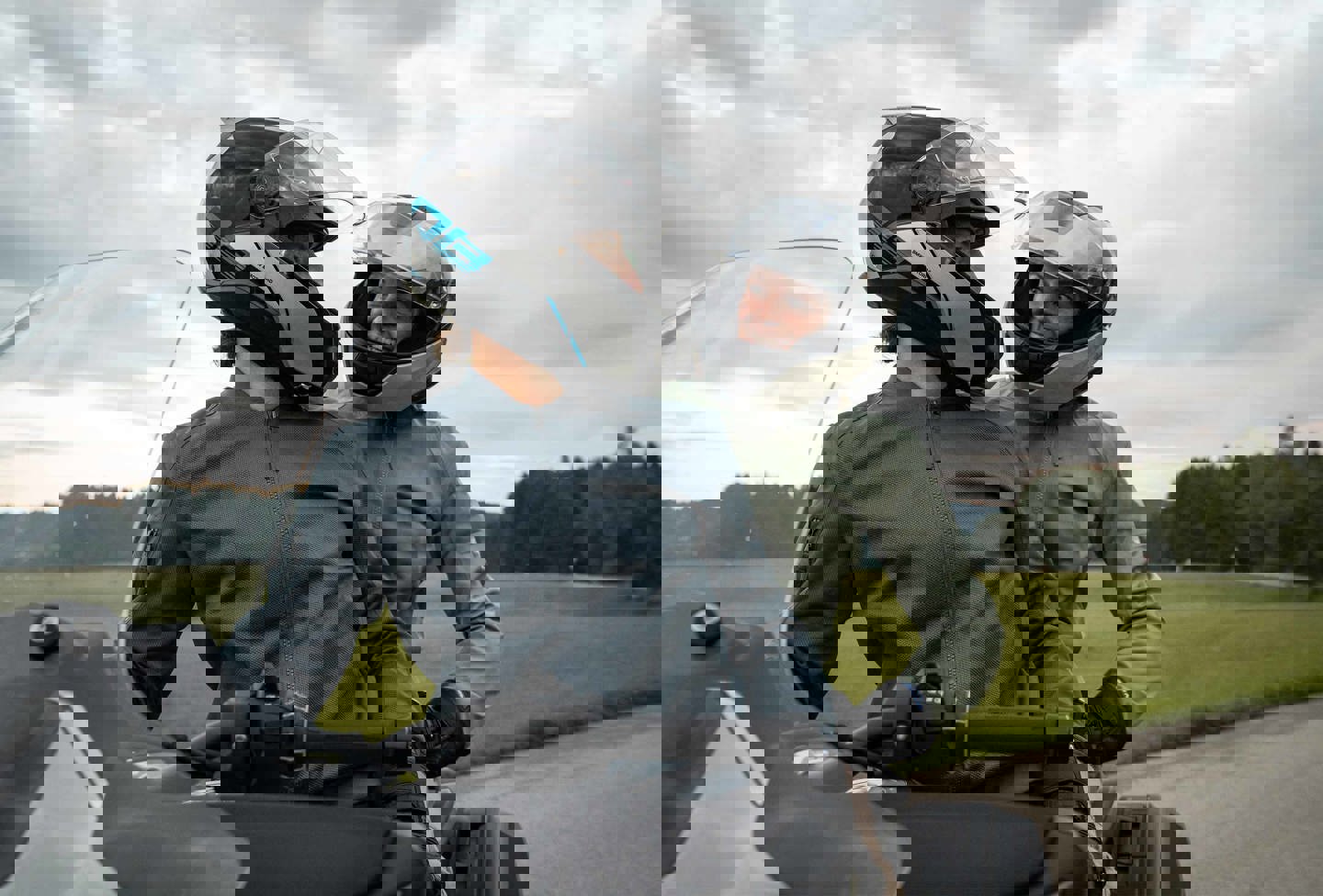 To personer sidder på en parkeret motorcykel med motorcykelhjelm på, mens de kigger på hinanden og smiler.