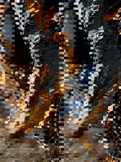 Et nærbillede af et ben med en blå og sort motorcykelstøvle med jord på, der støtter på pedalen.