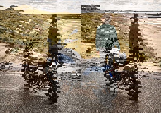 En person kører på motorcykel på en vej i nærheden af en strand.