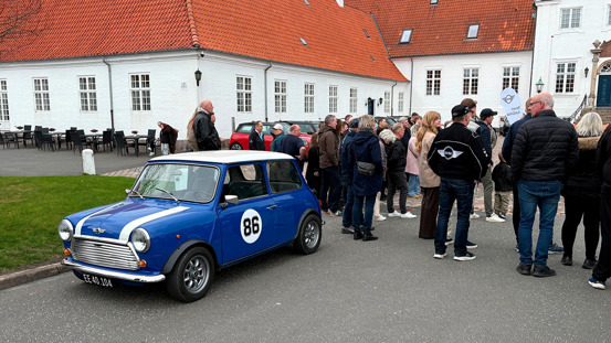 En blå klassisk Mini Cooper med et hvidt nummer 86 er parkeret, mens folk samles uden for Comwell Hotel Bygholm Park til Mini Spring Drive 2026.