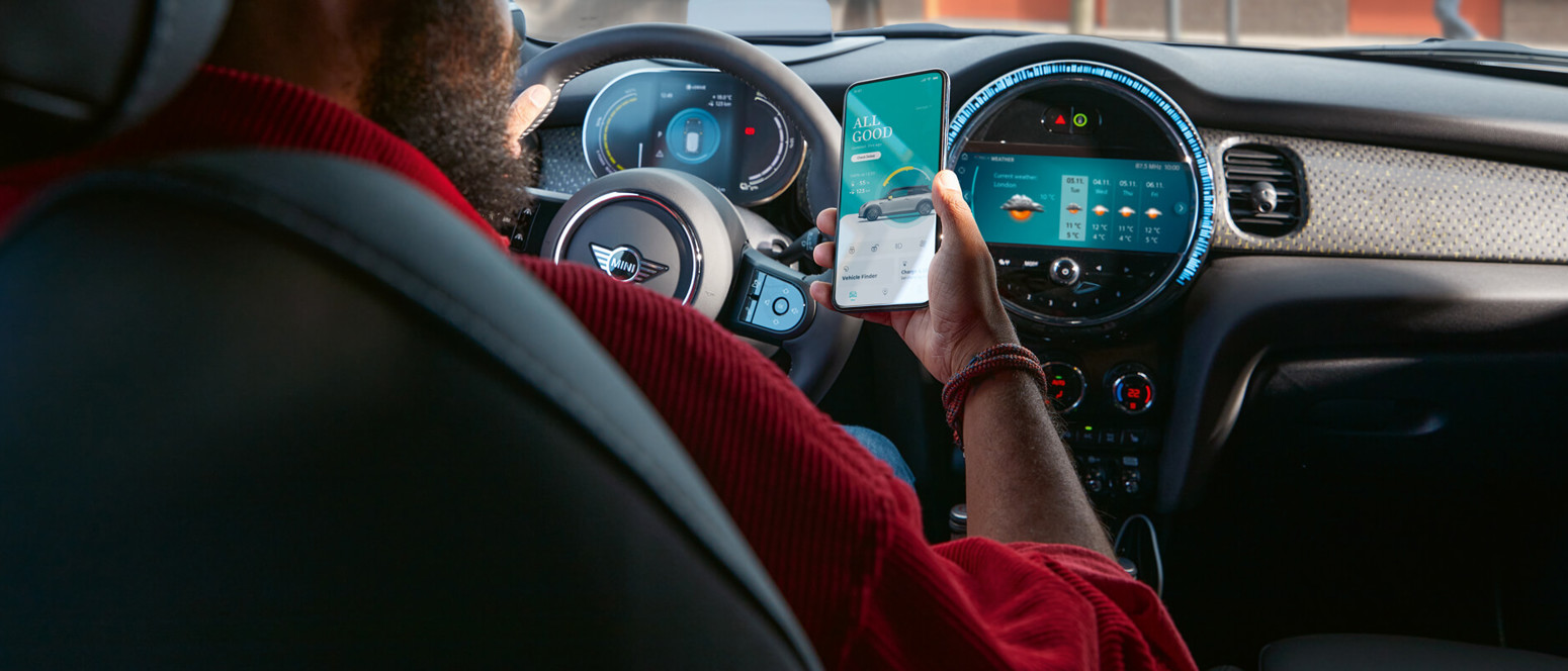 MINI-ejer på førersædet af sin MINI benytter MINI app på sin smartphone 