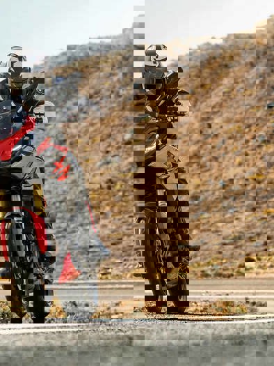 En person der kører på en rød og sort BMW motorcykel på en vej i et bjerglandskab.